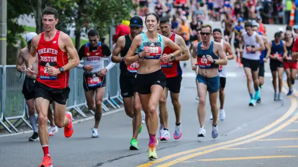 Runners in a marathon, some wearing "Greater Boston" gear, push through the race. The image captures the intensity of the iron man marathon length.
