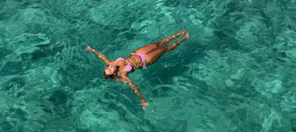 A woman in a pink bikini floats on her back in clear turquoise water. She's enjoying the water, and yes, you can swim with a tampon.