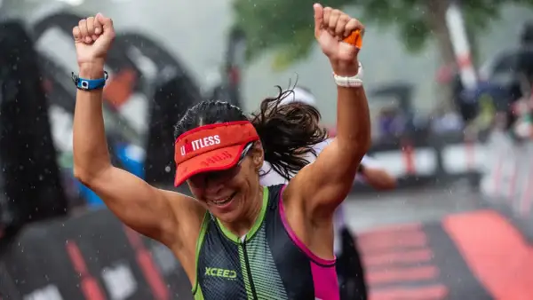 A triumphant athlete celebrates crossing the finish line of an Ironman length race in the rain.
