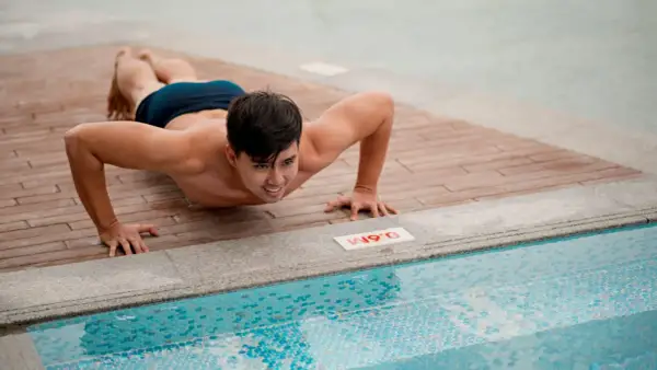 Man doing push-ups on a wooden deck next to a swimming pool.