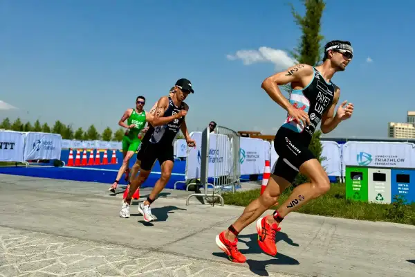 Triathletes push hard on the run course, a key part of their sprint tri training plan. Bright sun, blue skies, and a competitive spirit.