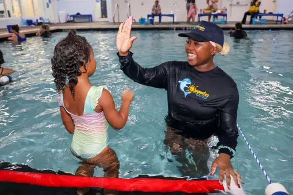 A swim instructor gives a young girl a high-five during swim stroke lessons.