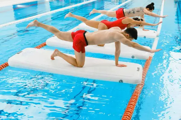 Three people practice aqua gym on inflatable mats in a pool, balancing in a plank-like pose.