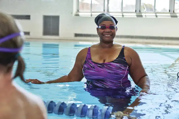 Smiling woman in a purple swimsuit and swim cap enjoys swim lessons for seniors.