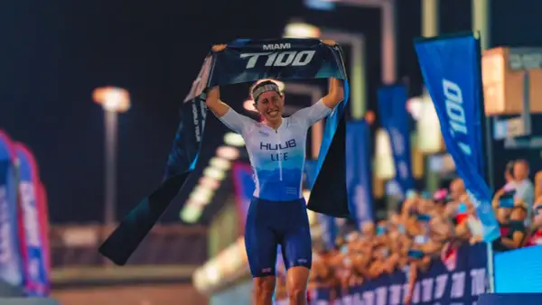 India Lee celebrates a victory, holding up a "Miami T100 World Tour" banner.