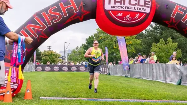 A woman crosses the finish line at a triathlon, smiling. This event is one of the best triathlons for participants to achieve their goals.