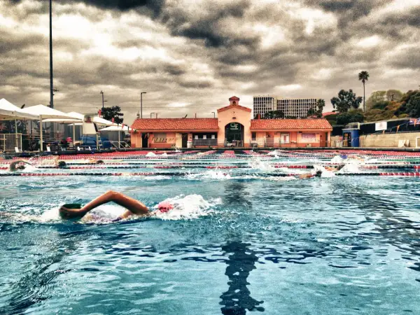 Swimmers race in an outdoor pool under a dramatic cloudy sky, enjoying a refreshing morning swim.