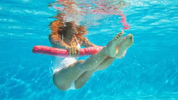 Underwater view of a woman doing pool workouts for weight loss, holding a pink noodle for support.