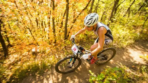Athlete races through an autumn forest during an off road triathlon, navigating a dirt path with colorful foliage.
