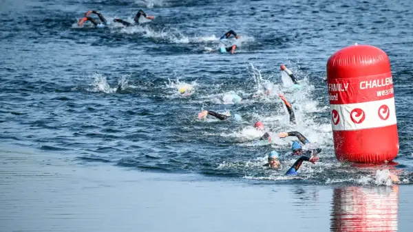 Athletes compete in a triathlon, their triathlon swim strokes creating splashes as they navigate the water around a red buoy.