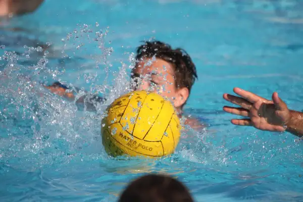 A young player in a water polo match splashes water as they go for the ball.