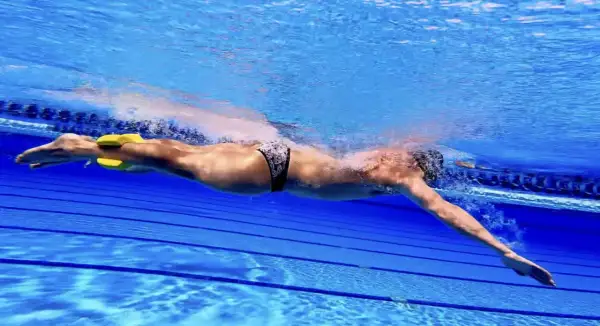 Swimmer using a pull buoy between legs to isolate arm stroke. This technique helps improve upper body strength and efficiency, demonstrating how to use a pull buoy effectively.