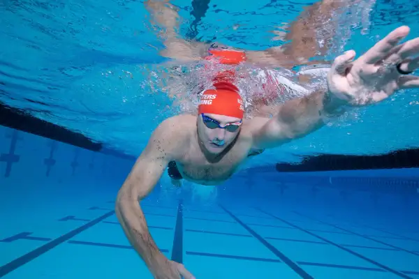 Underwater view of a swimmer performing a freestyle swim stroke, with arms extended and water splashing around.