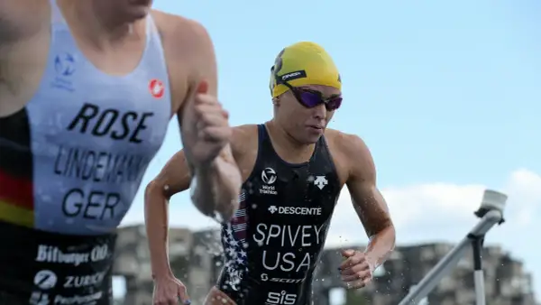 Taylor Spivey, a triathlete in a yellow cap and goggles, emerges from the water, her USA suit glistening.