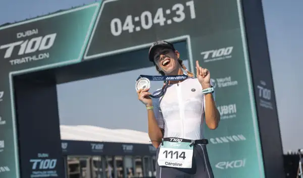Caroline celebrates her finish at the Dubai T100 Triathlon, medal in hand, under the finish arch.