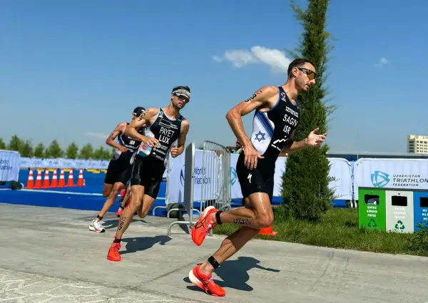 Athletes in racing gear push forward during a triathlon training run, focused and determined under a bright blue sky.