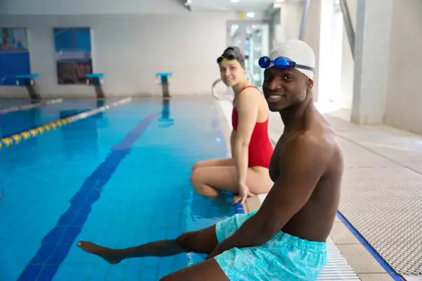 Smiling adults in swim gear at pool edge, ready for swim lessons for adults with fear of water.