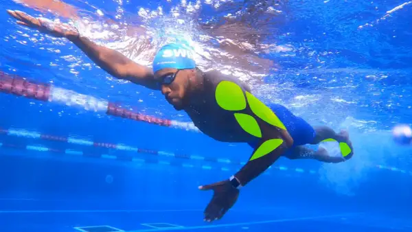 Swimmer in blue cap and goggles, with neon green markings on his body, powerfully pulls through the water in a lane.