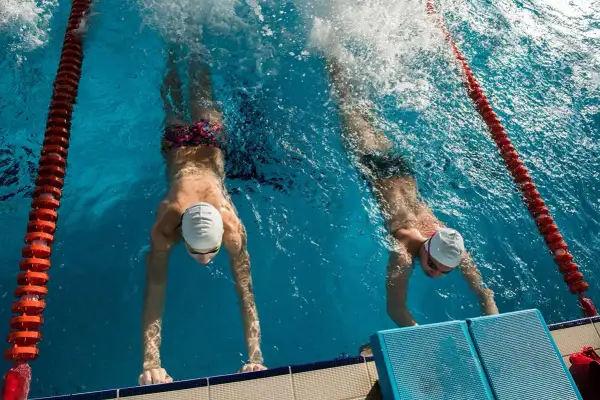 Two swimmers practice their flutter kicks, pushing off the wall in a race.