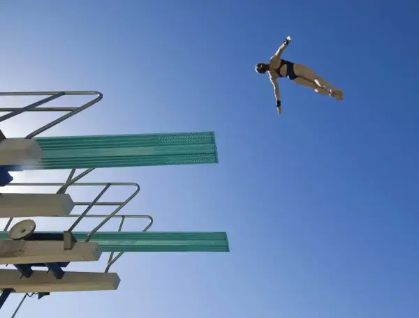A diver in mid-air, performing a competitive dive against a clear blue sky.