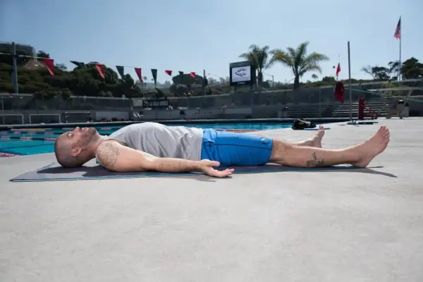 Man practicing yoga for swimmers, lying on a mat by the pool, enjoying a moment of relaxation and recovery.