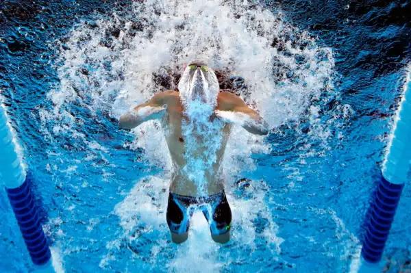 Swimmer powering through intense swim practice sets, creating a splash as they break the water's surface.