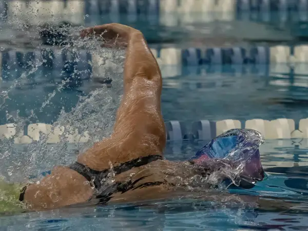 A swimmer's arm slices through the water, demonstrating the powerful stroke needed to swim laps. Water splashes around them as they focus on their technique.