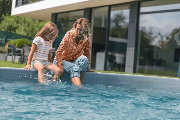 A mother and daughter sit by a pool, splashing their feet. They're enjoying a sunny day, and the daughter asks, "Can you swim with mono?