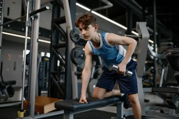 Young swimmer performing dumbbell rows as part of their cross training routine in a gym.